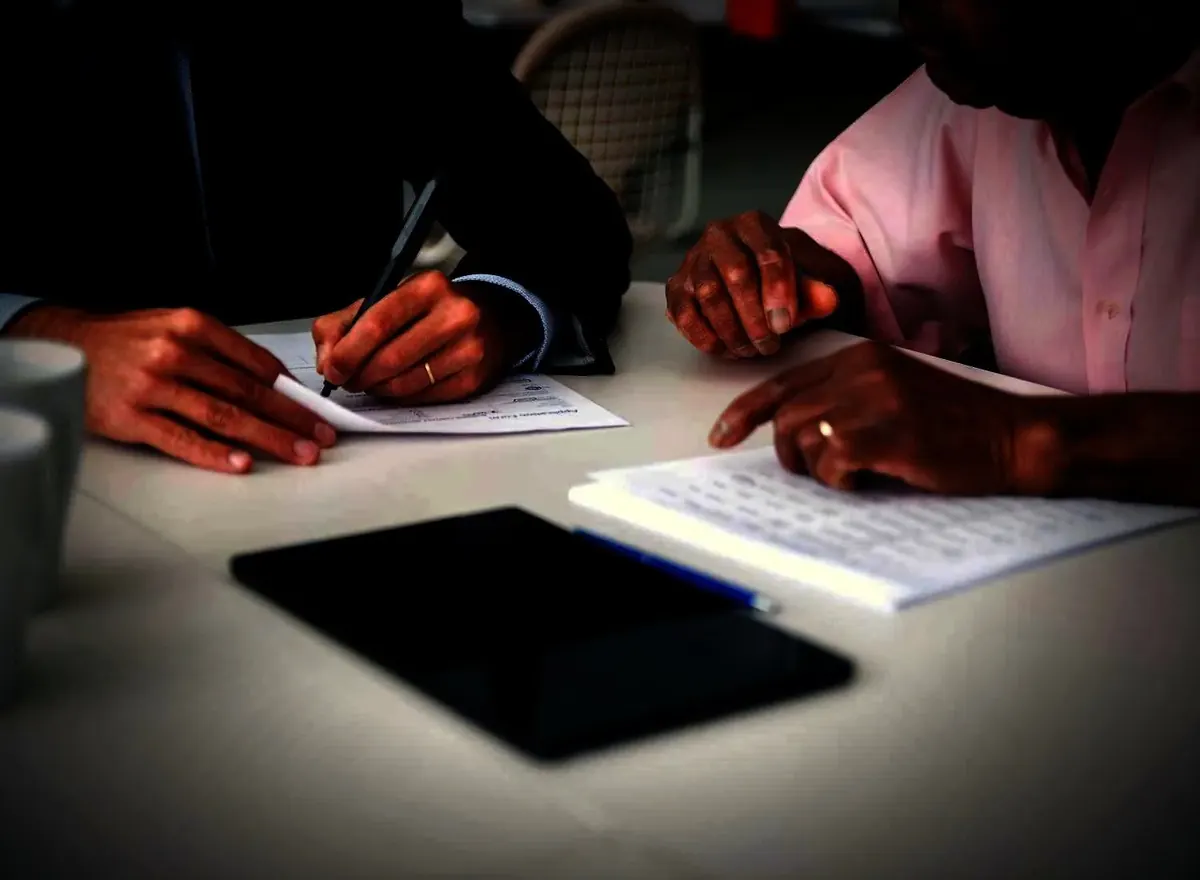 Duas pessoas assinando documento em reunião