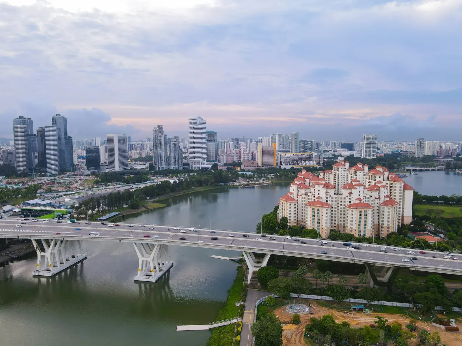 Vista aérea de uma cidade ao entardecer, com ponte, lago e prédios